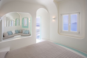 Ein modernes Hotelzimmer mit Bett, einer Sitzecke mit Kissen, einem Balkon mit Aussicht und einem großen Fenster.