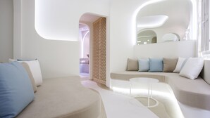 A modern living room with a curved sofa, a small round coffee table, and a decorative partition. - Andronikos Santorini (Santorini)