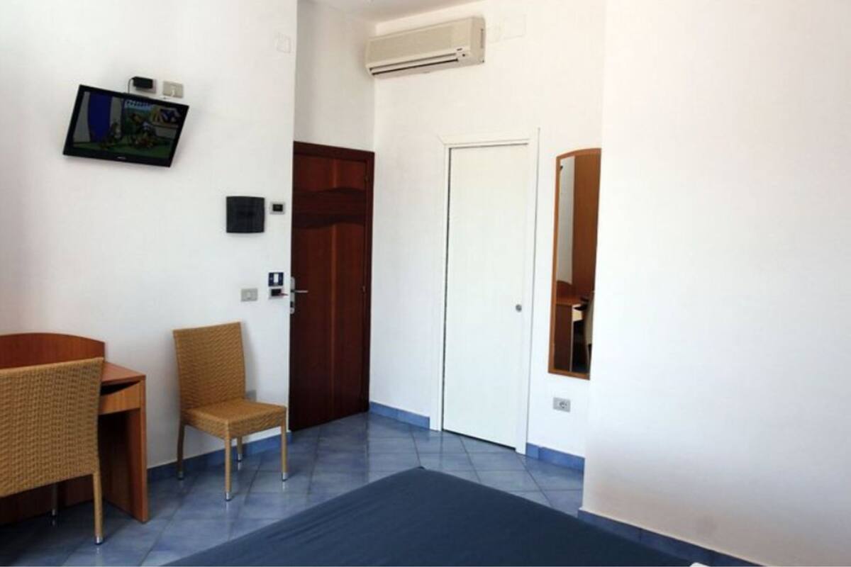 A small room with a desk, two wicker chairs, a door, and a wall-mounted TV.