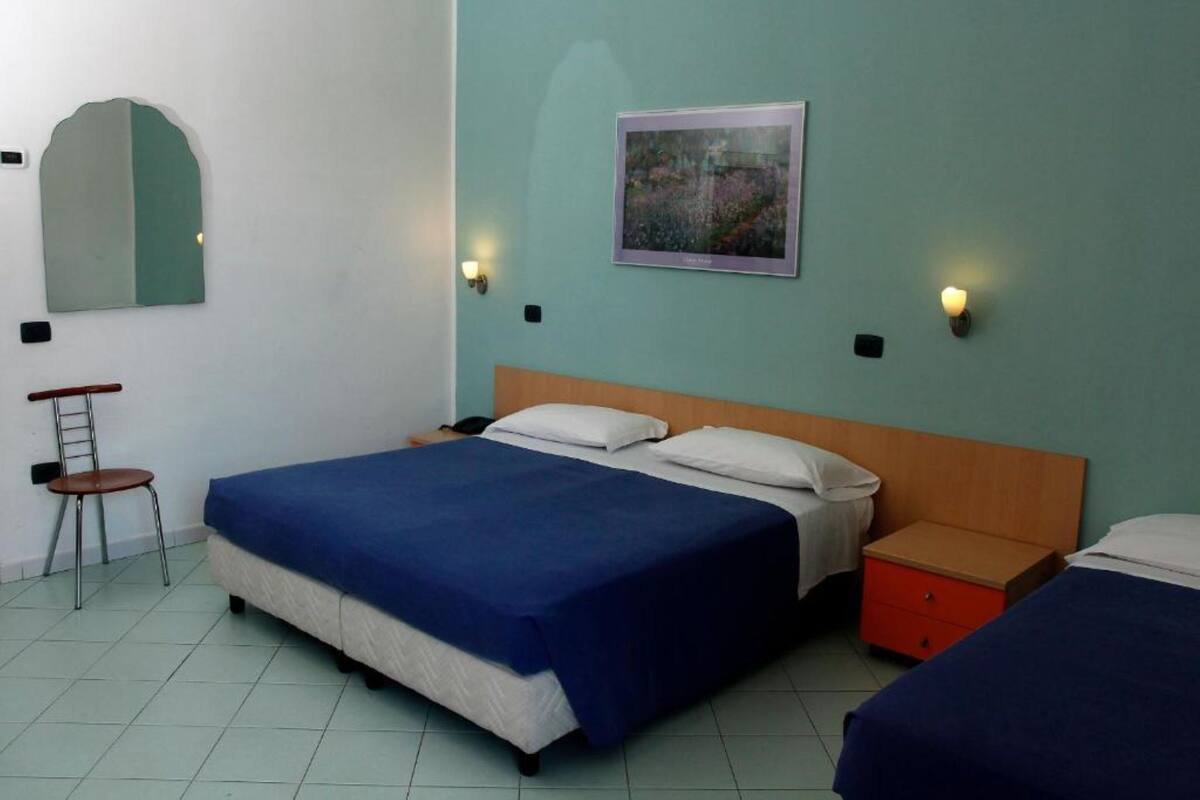A bedroom with a large bed, two bedside tables, a chair, and a painting on the wall.