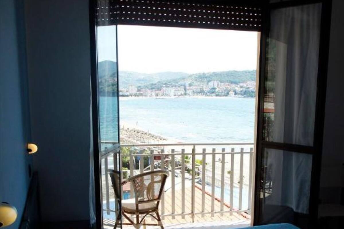 A bedroom with a bed, a chair, and a view of a beach and water.