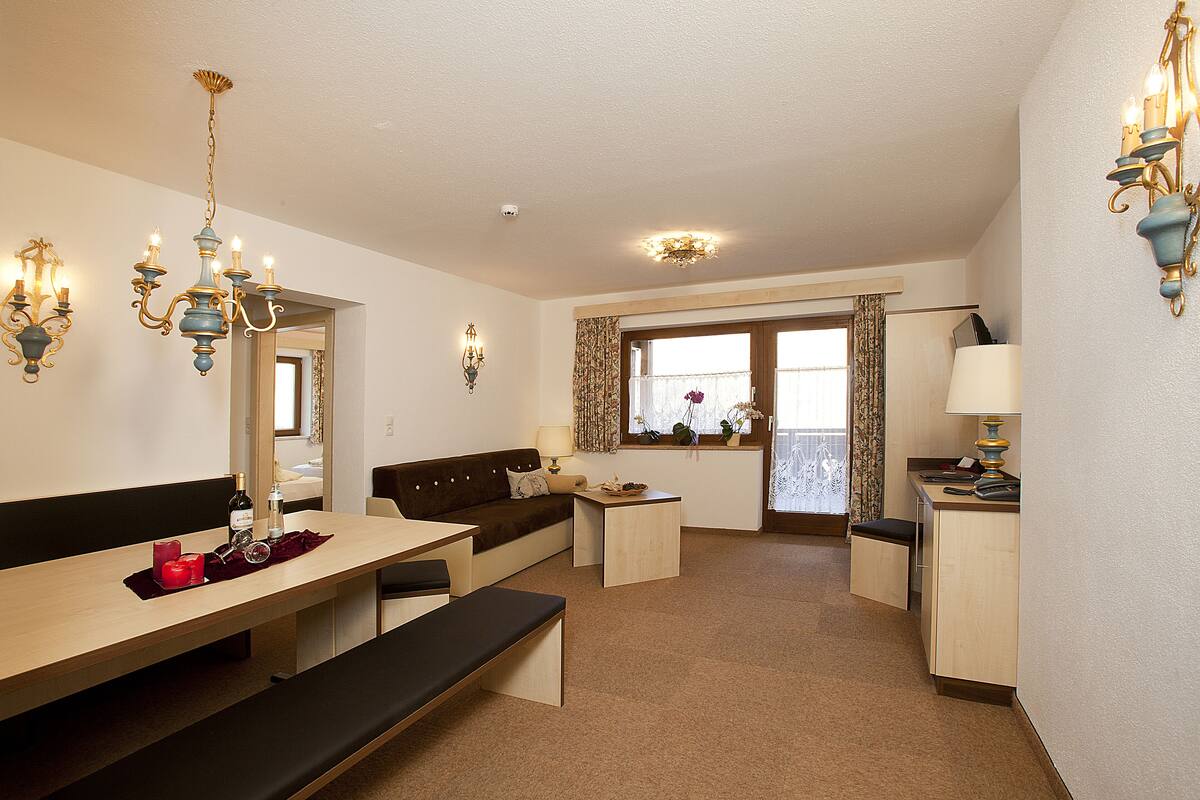 Ett hotellrum med en matplats, en soffa, en bänk, ett skrivbord och ett fönster med gardiner.
