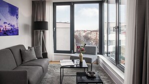Una sala de estar moderna con un sofá gris, una mesita con un jarrón y vistas a la ciudad a través de amplios ventanales.
