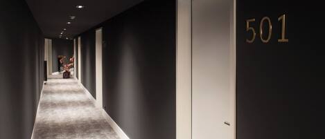 A hallway with a carpeted floor, dark walls, and a door marked with the number 501.