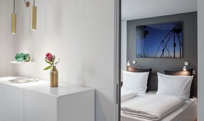 A modern bedroom with a bed, bedside lamps, a nightstand, and a wall-mounted painting. - AMANO HOME Apartments (Berlin)