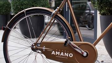 Bicicleta com quadro marrom e etiqueta com a inscrição "HOTEL AMANO", estacionada em frente a um edifício.