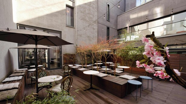 Un patio al aire libre con mesas, sillas de madera y luces colgantes.