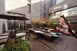 An outdoor patio with wooden seating, tables, and string lights. - AMANO HOME Apartments (Berlin)