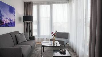 A modern living room with a grey sofa, a coffee table, and a floor lamp. There is a painting on the wall and a window with sheer curtains.