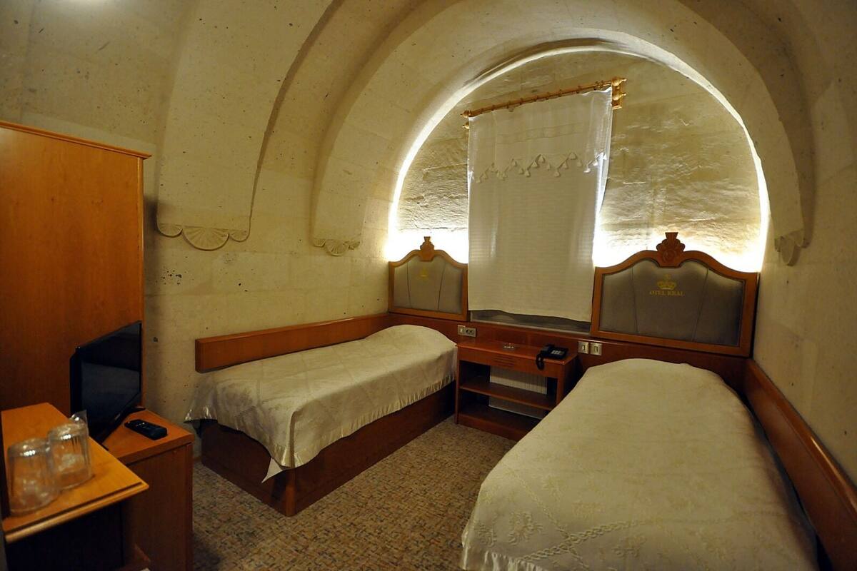 A small, cozy room with two single beds, a wooden desk, a chair, and a large arched window with a curtain.