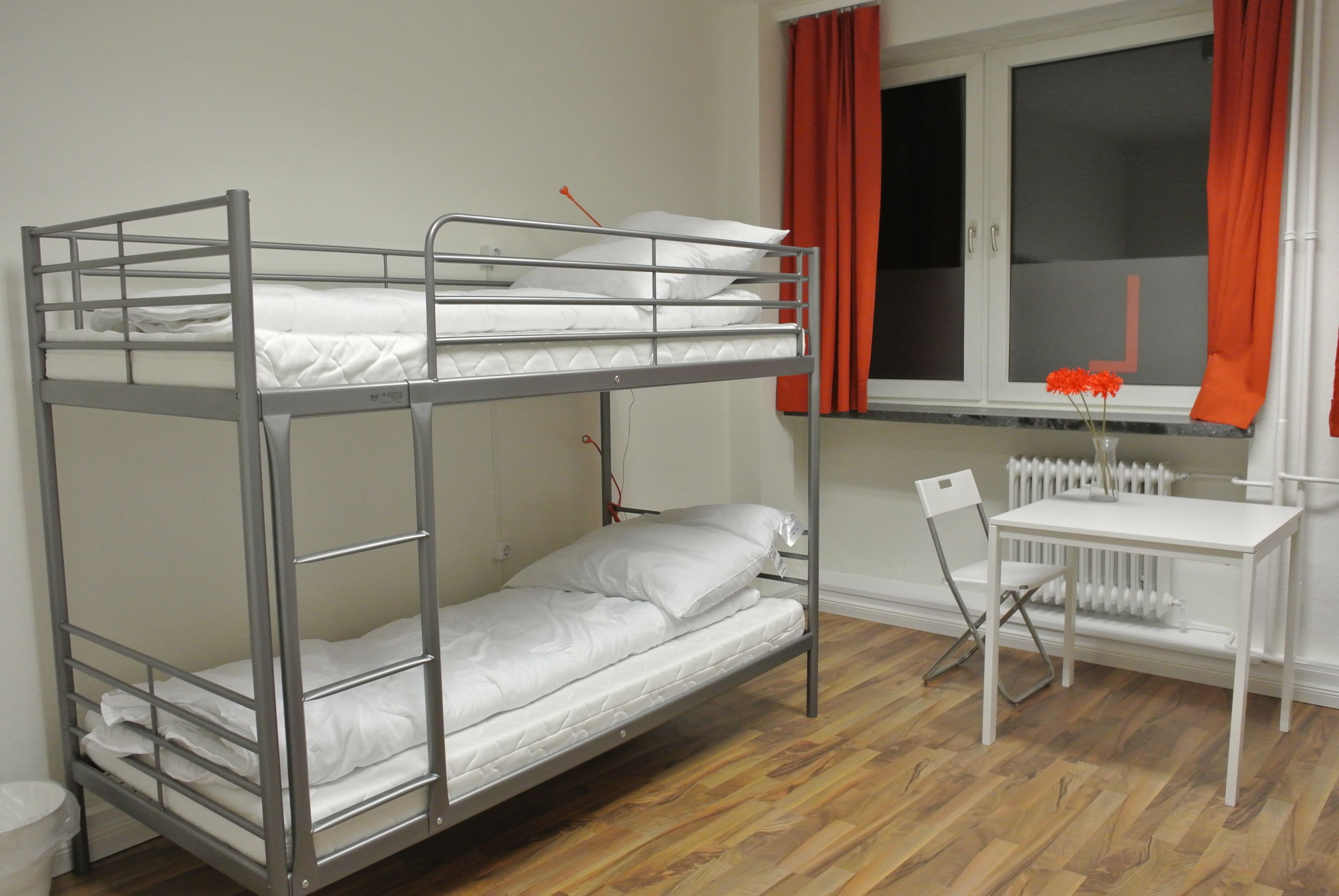 A bunk bed with a desk and chair, a radiator, and a window with curtains.
