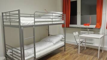 A bunk bed with a desk and chair, a radiator, and a window with curtains.