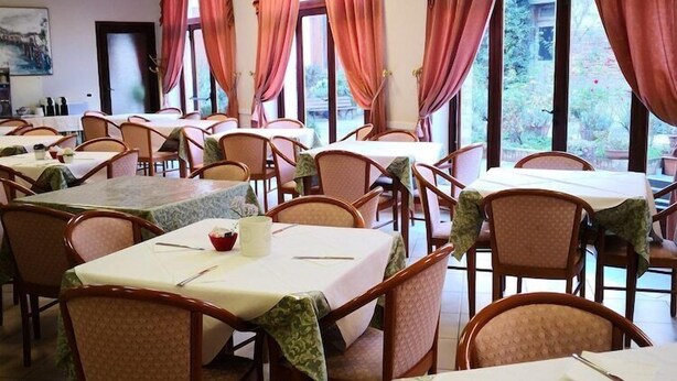 A dining area with tables and chairs, large windows with curtains, and a painting on the wall. - Domus Ciliota (Venice)