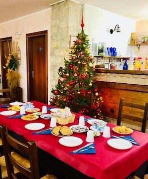 A dining area with a red tablecloth, a Christmas tree, and a stone wall. - Le Coccole (Guardiaregia)