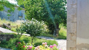 En bygning i sten med et tag af fliser, omgivet af frodigt grønt og blomstrende planter.