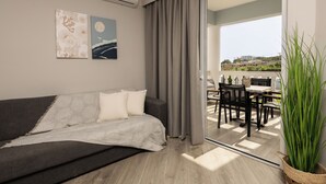 Una sala de estar moderna con un sofá, una mesa de comedor y sillas. Se ve un ventanal con cortinas, y una planta.