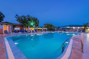 Una piscina con sillas de descanso y sombrillas, rodeada de edificios y árboles.