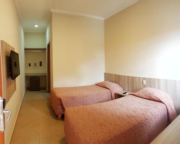 A hotel room with two beds, a TV mounted on the wall, and a small kitchenette in the background. - Éden Park Hotel (Sorocaba)