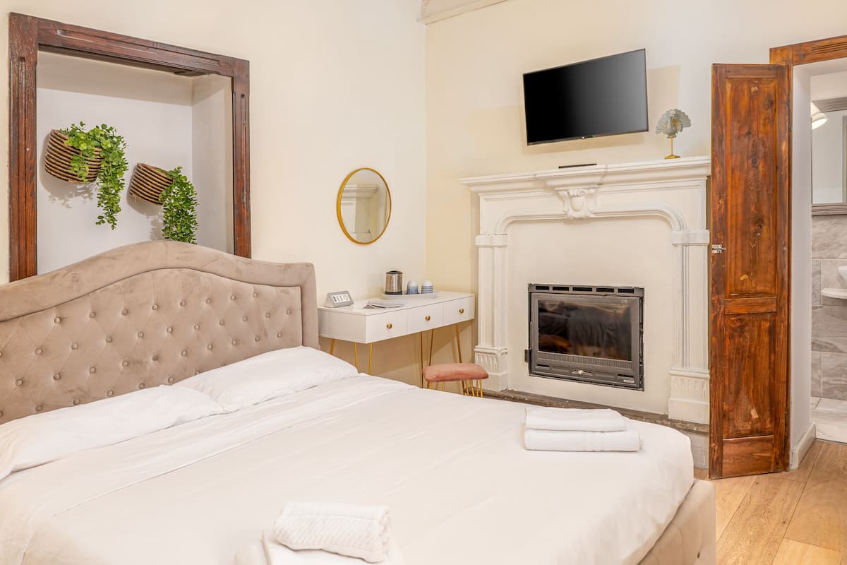 Een slaapkamer met een groot bed, een nachtkastje met een telefoon en een lamp, een open haard, en een tv die erboven hangt.