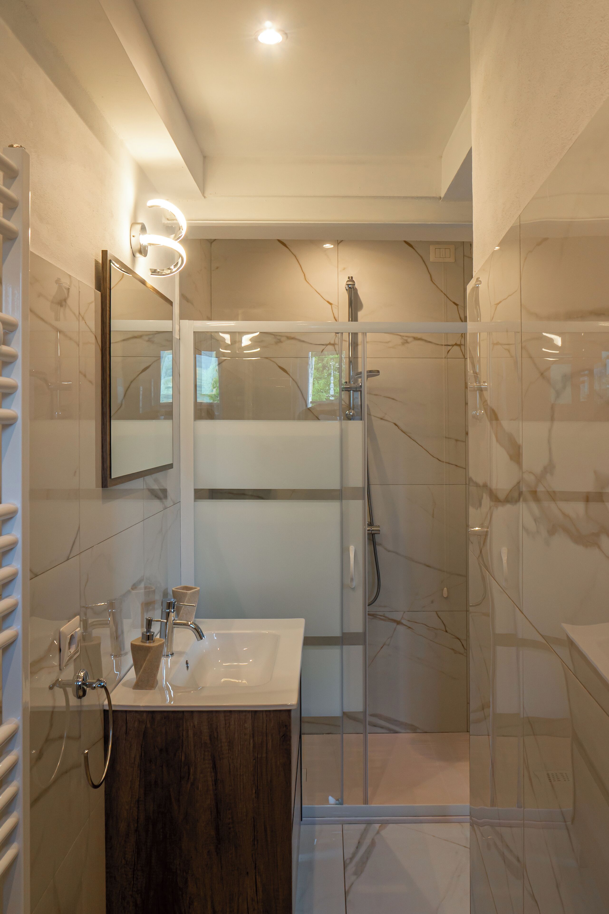 A modern bathroom with a glass shower enclosure, a vanity with a marble countertop, and a wall-mounted mirror with lights.