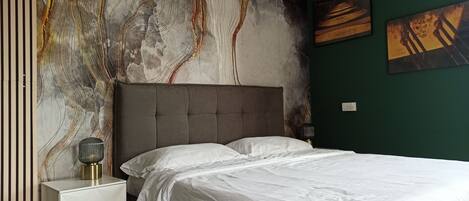 Une chambre avec un grand lit, une table de chevet et un mur orné d’œuvres d’art abstraites.
