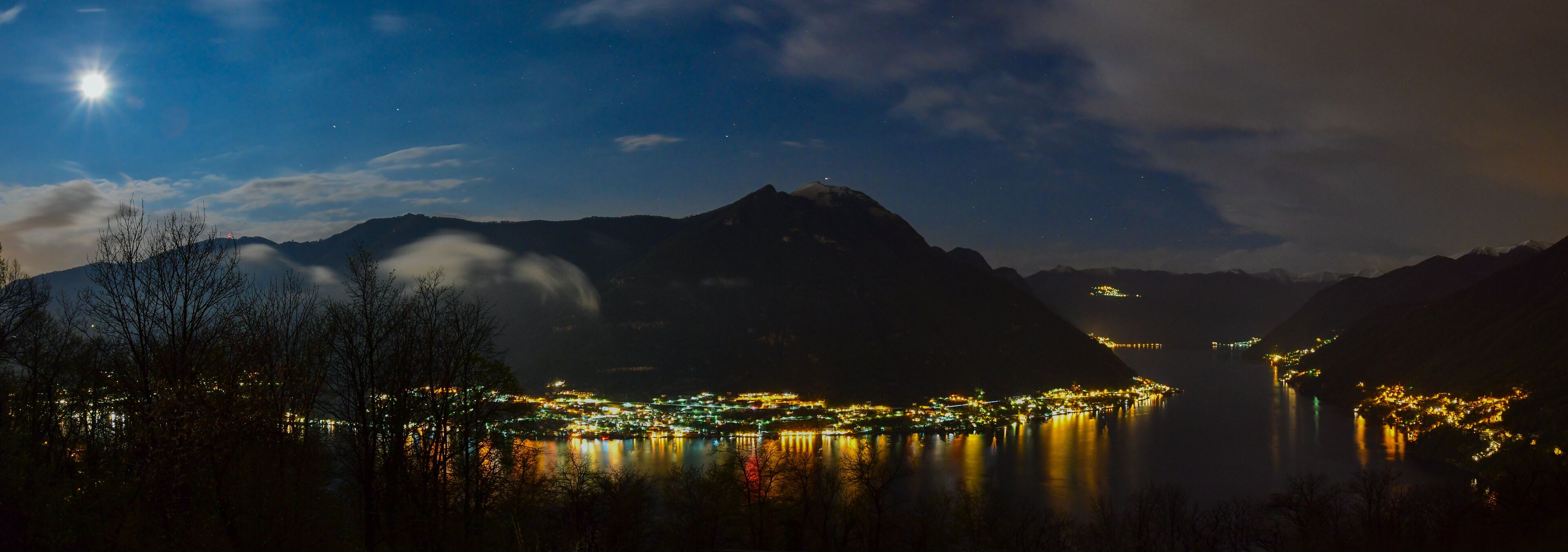 A nighttime view of a town by a lake with mountains in the background.