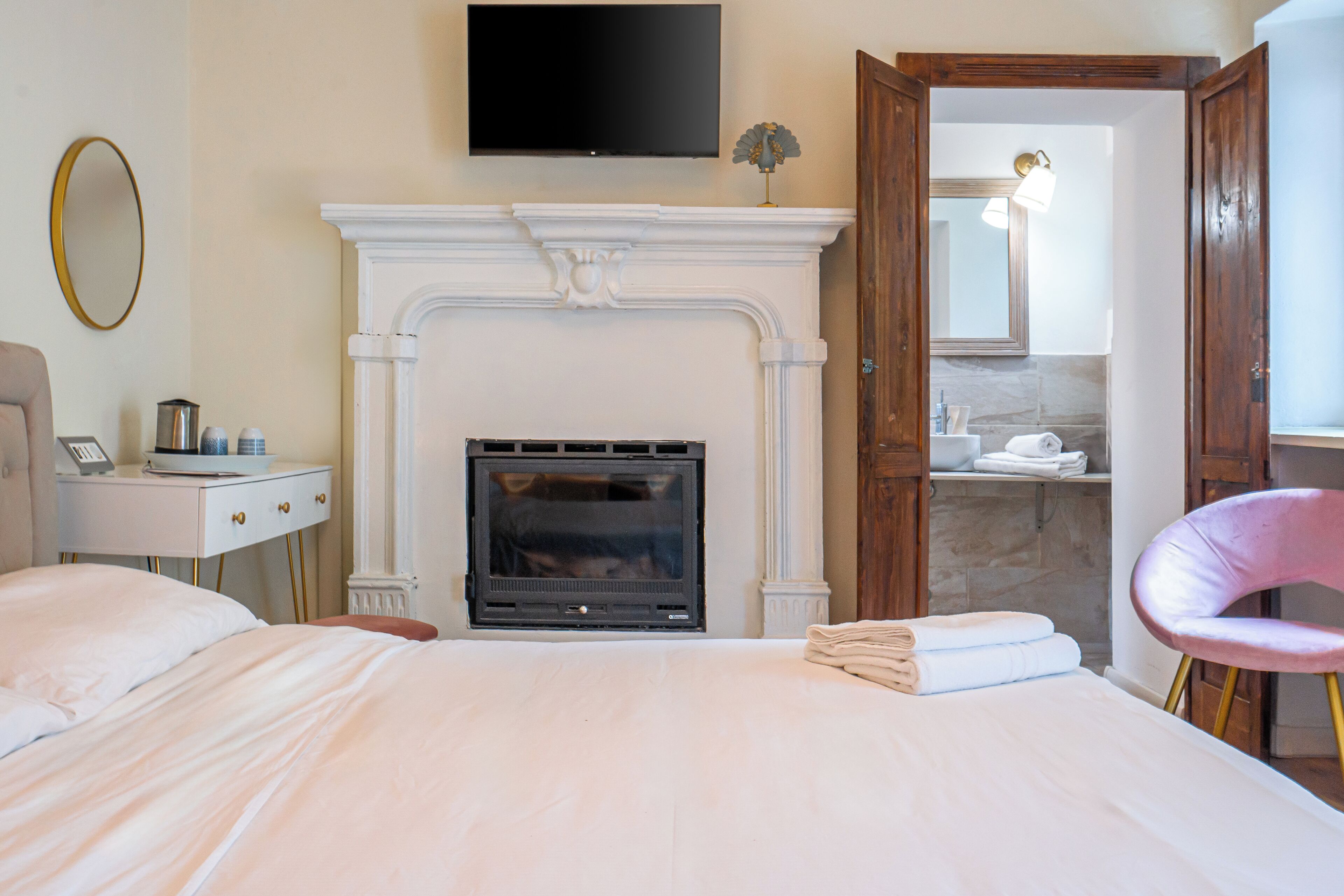 A bedroom with a fireplace, a television mounted above it, a bedside table with a lamp, and a bathroom visible through an open door.