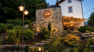 A stone building with a neon sign, outdoor lighting, and a staircase leading to a covered area.