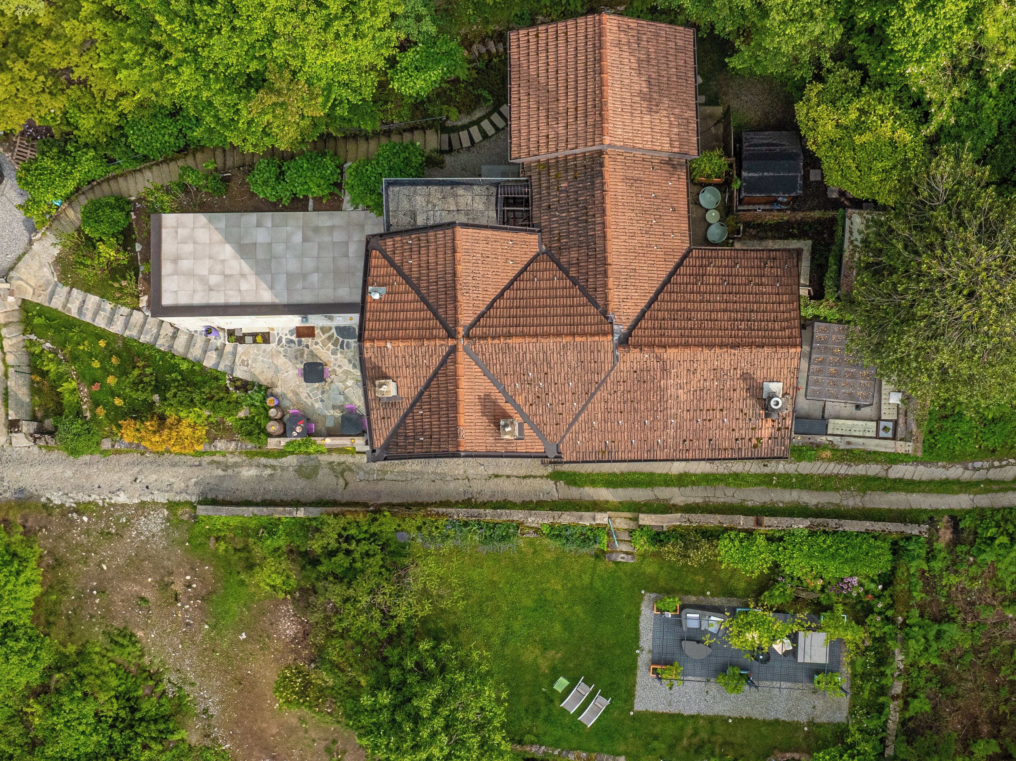 Eine Vogelperspektive eines Gebäudes mit einer markanten, geometrischen Dachkonstruktion, umgeben von Grünflächen und einer Steinmauer.
