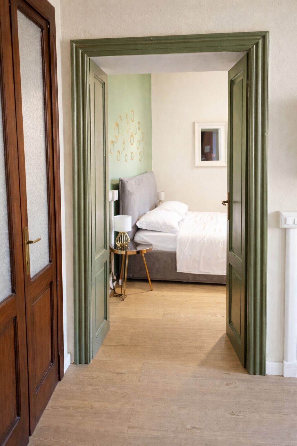 A bedroom with a bed, a bedside table, a lamp, and a wall with circular patterns.