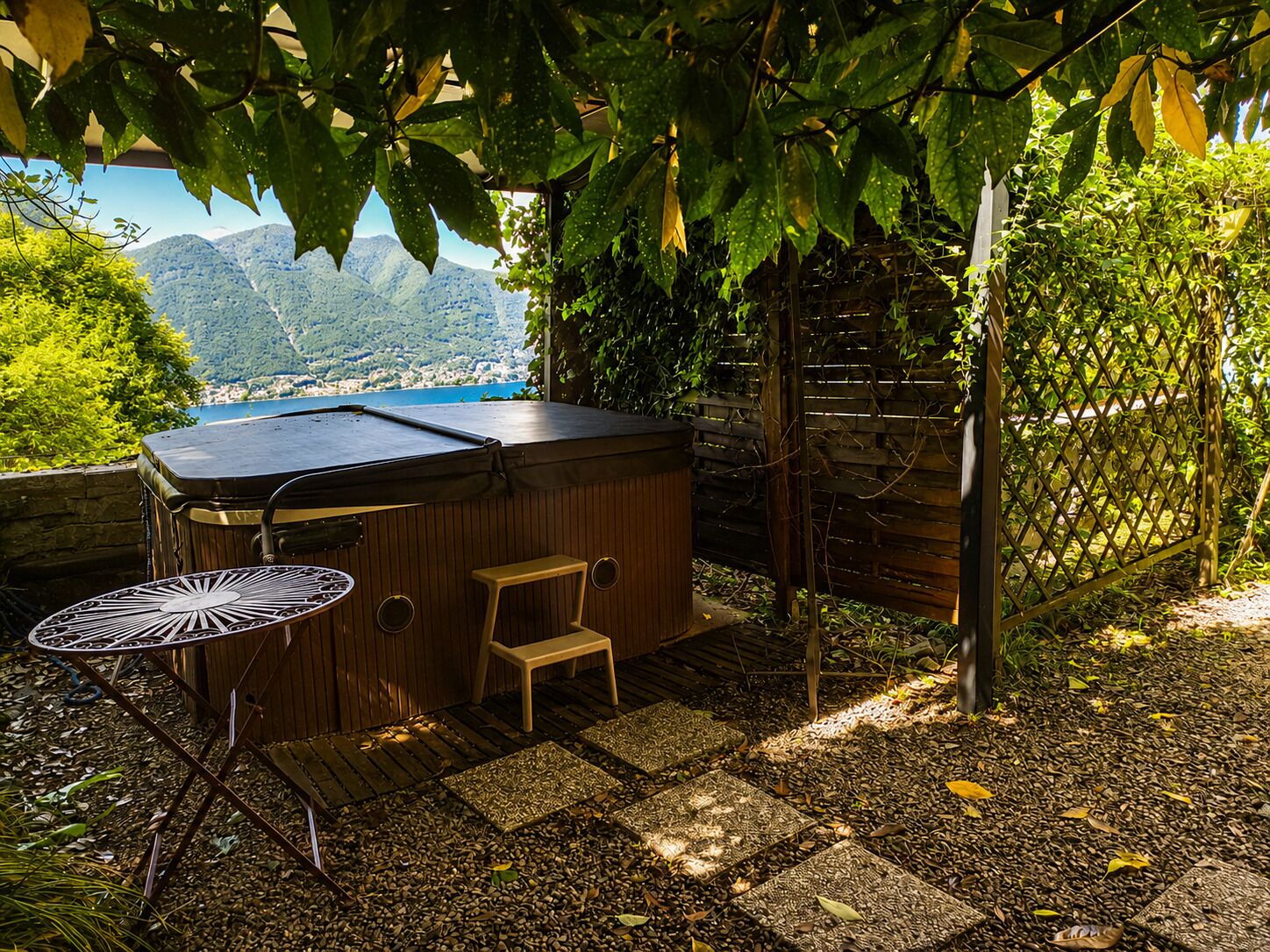 A hot tub under a pergola with a view of mountains and a lake.