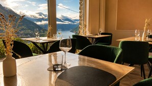 A restaurant with tables and chairs, a vase with dried plants, and a scenic mountain view. - Essentia Guest House  (Faggeto Lario)