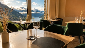 A restaurant with tables and chairs, a vase with dried plants, and a scenic mountain view.