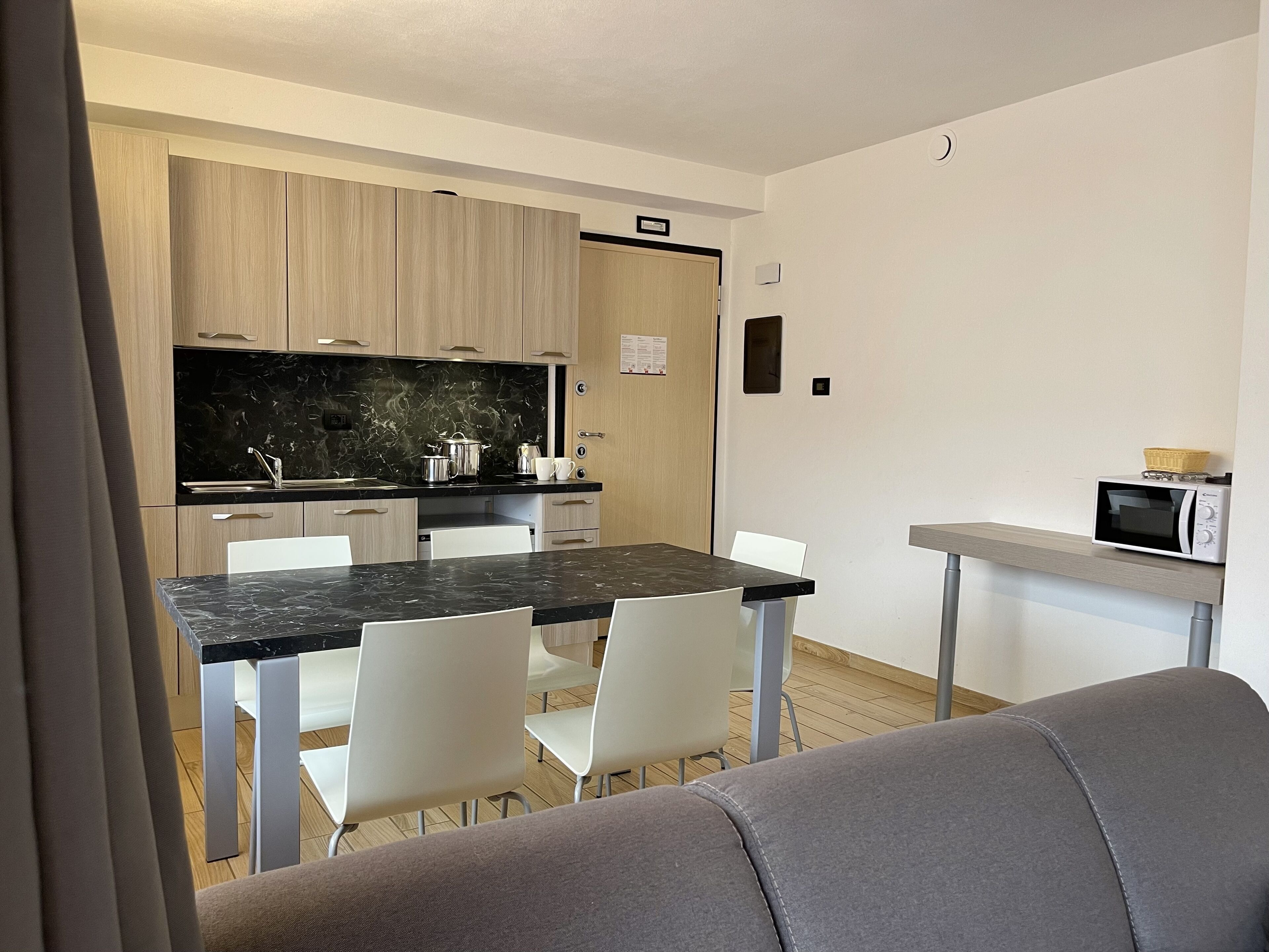 Une cuisine moderne avec un plan de travail noir, des chaises blanches et un micro-ondes posé sur une petite table.