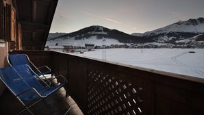 A balcony with a view of a snowy mountain landscape, a wooden railing, and two blue chairs. - Residence Adele (Livigno)