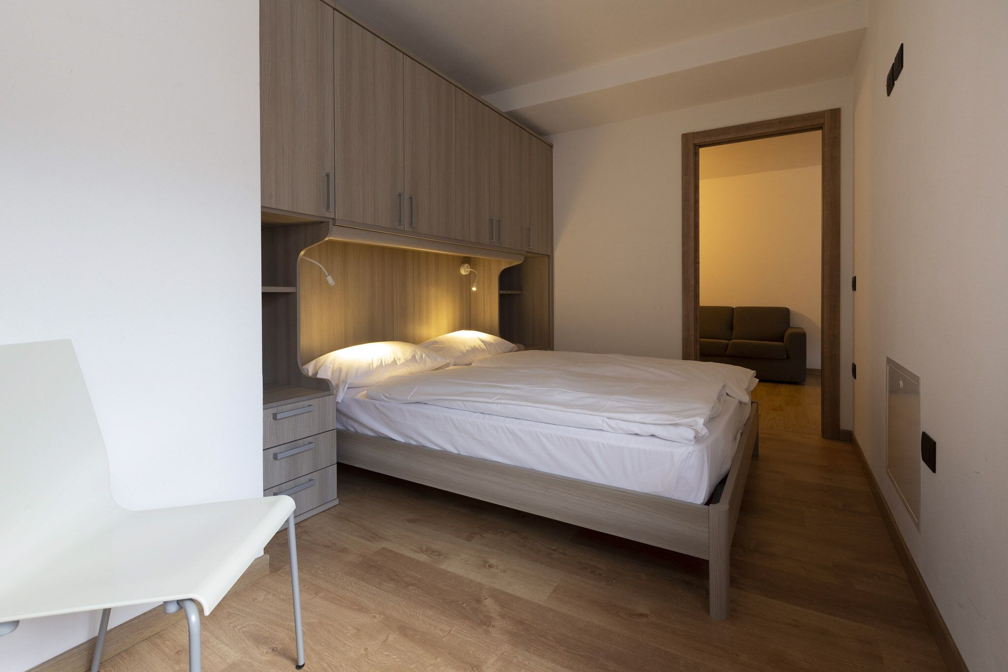 A bedroom with a bed, a bedside table, a chair, and a wardrobe.