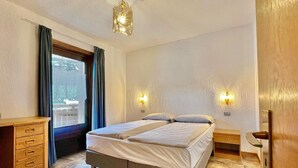 A bedroom with a bed, two bedside tables, a dresser, a window with curtains, and a ceiling light fixture. - Residence Adele (Livigno)