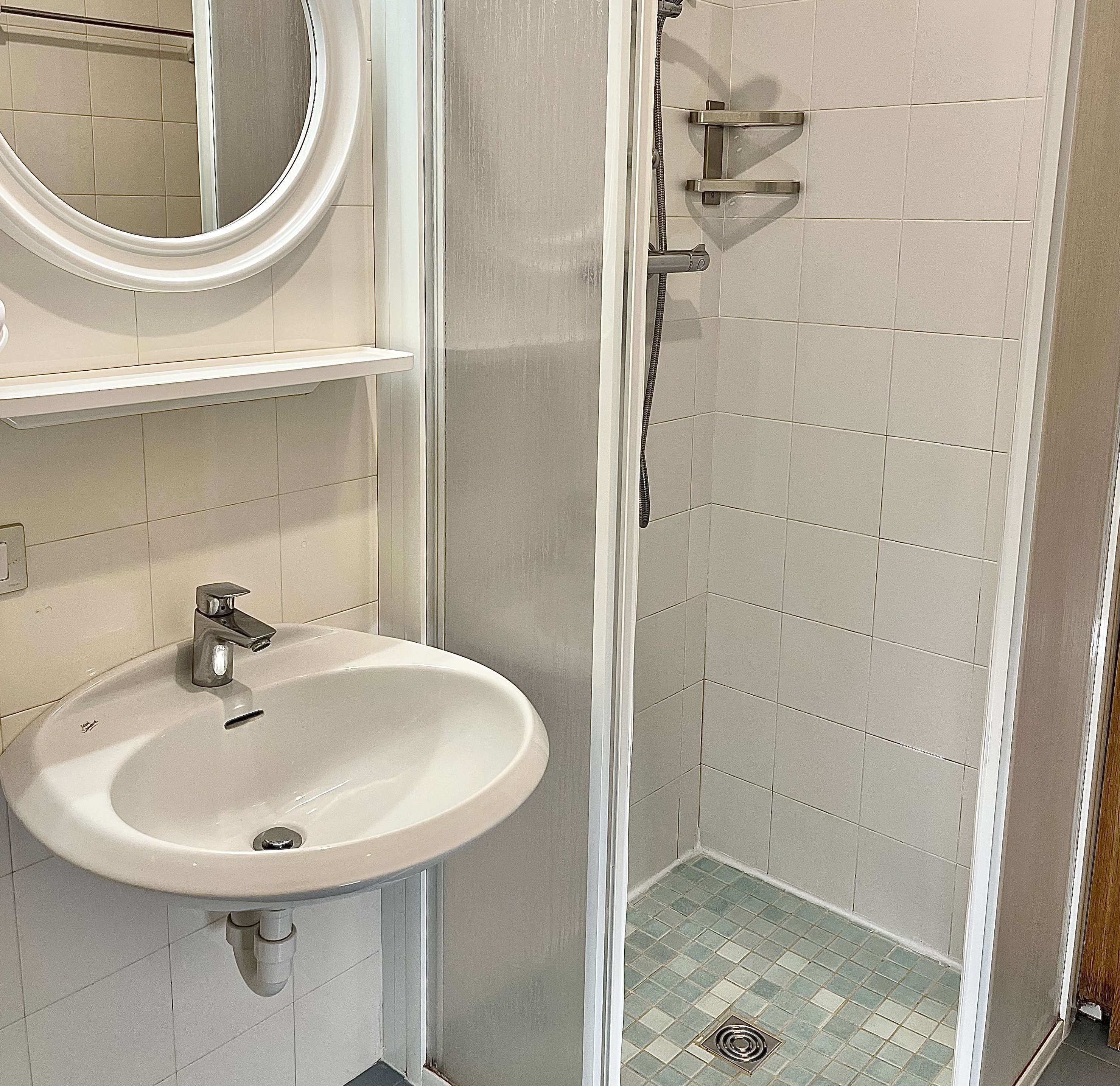 Een badkamer met een wit wastafel, een spiegel en een douche met betegelde wanden en vloer.