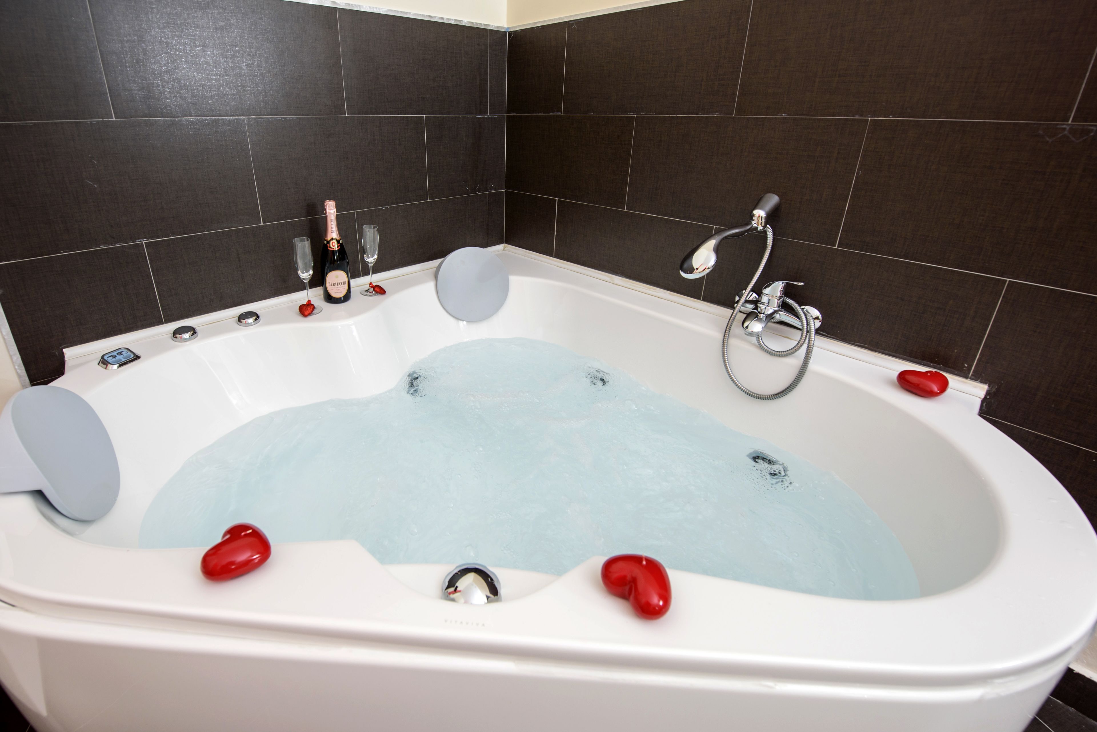 Une salle de bain moderne avec une grande baignoire, des murs recouverts de carreaux foncés et un espace douche.