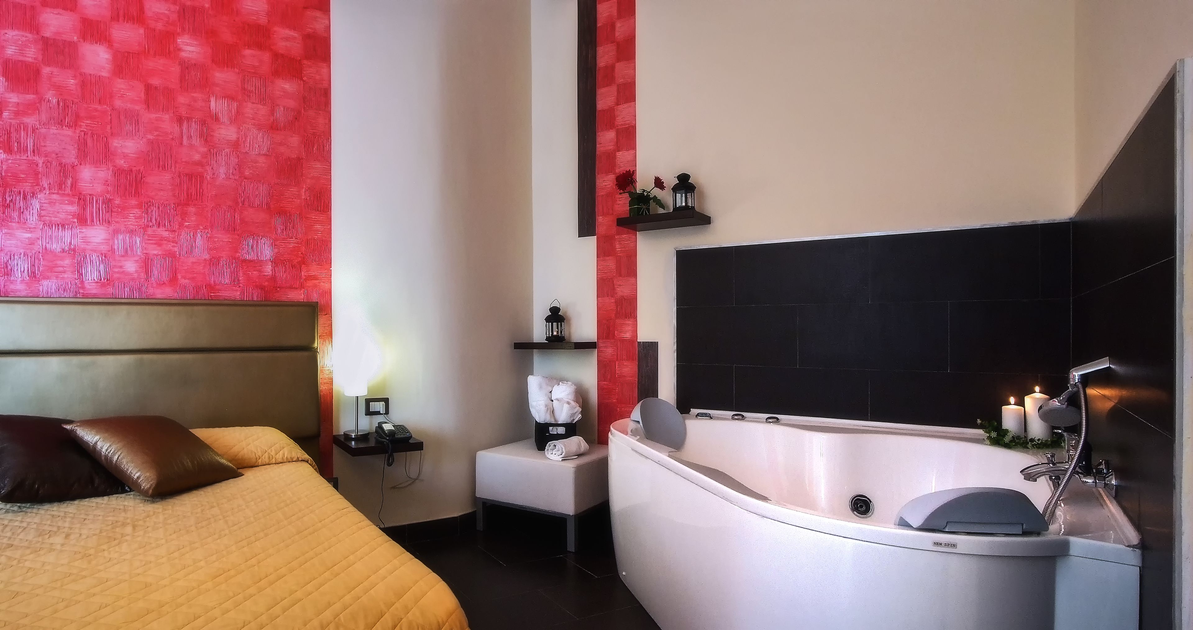 Habitación de hotel con cama, mesita de noche, lámpara, una pequeña mesa con teléfono, bañera blanca y espejo.