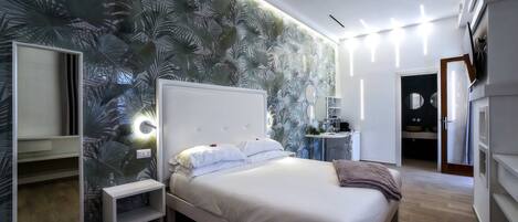 A modern bedroom with a large bed, a bedside table, a mirror, and a wall with a tropical leaf pattern.