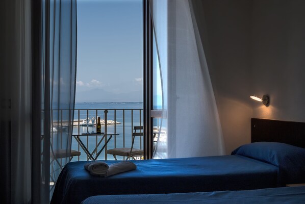 A hotel room with a bed, a table with chairs, and a view of the sea.