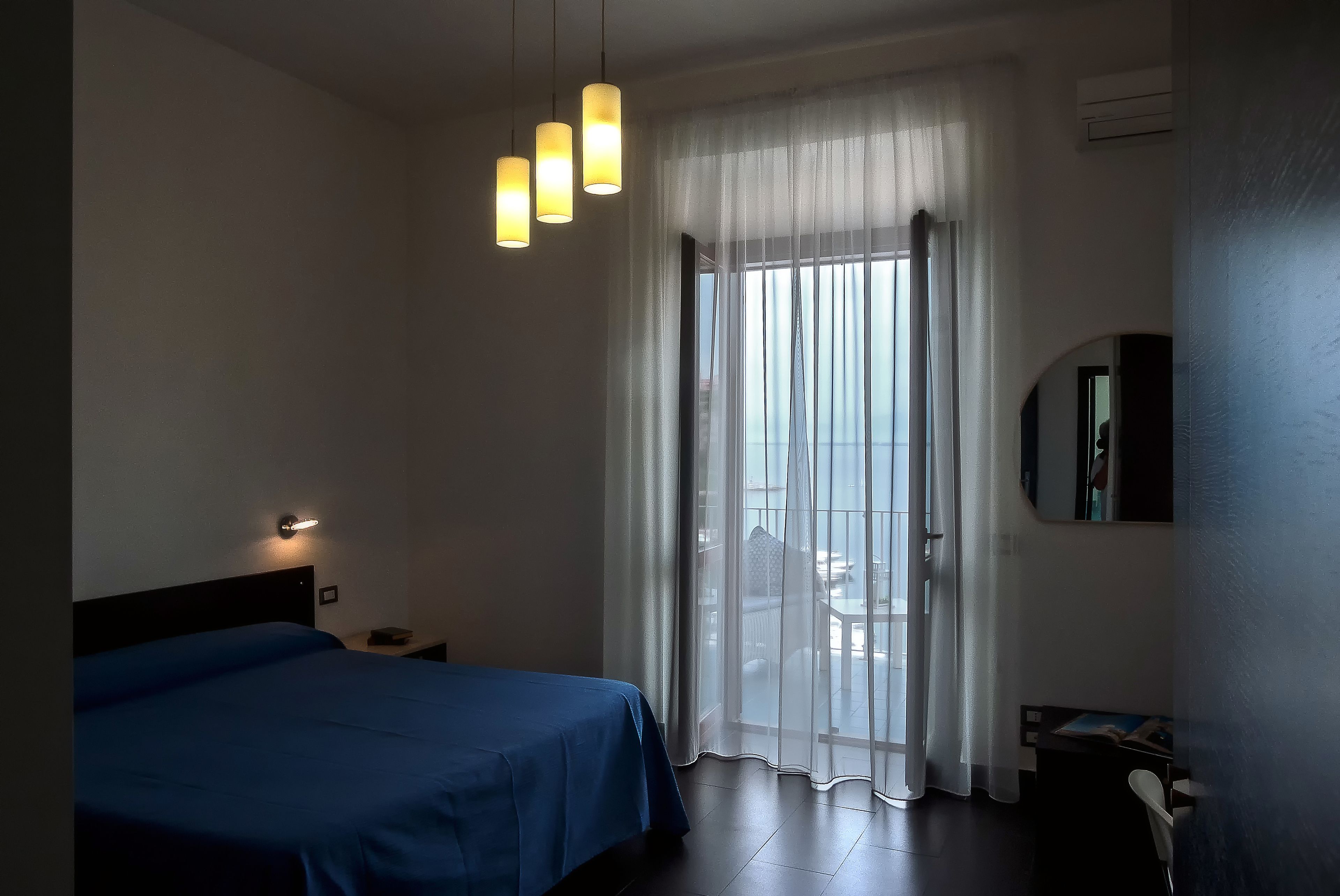 Habitación de hotel con cama, lámpara de noche y vista a través de una ventana con cortinas ligeras.