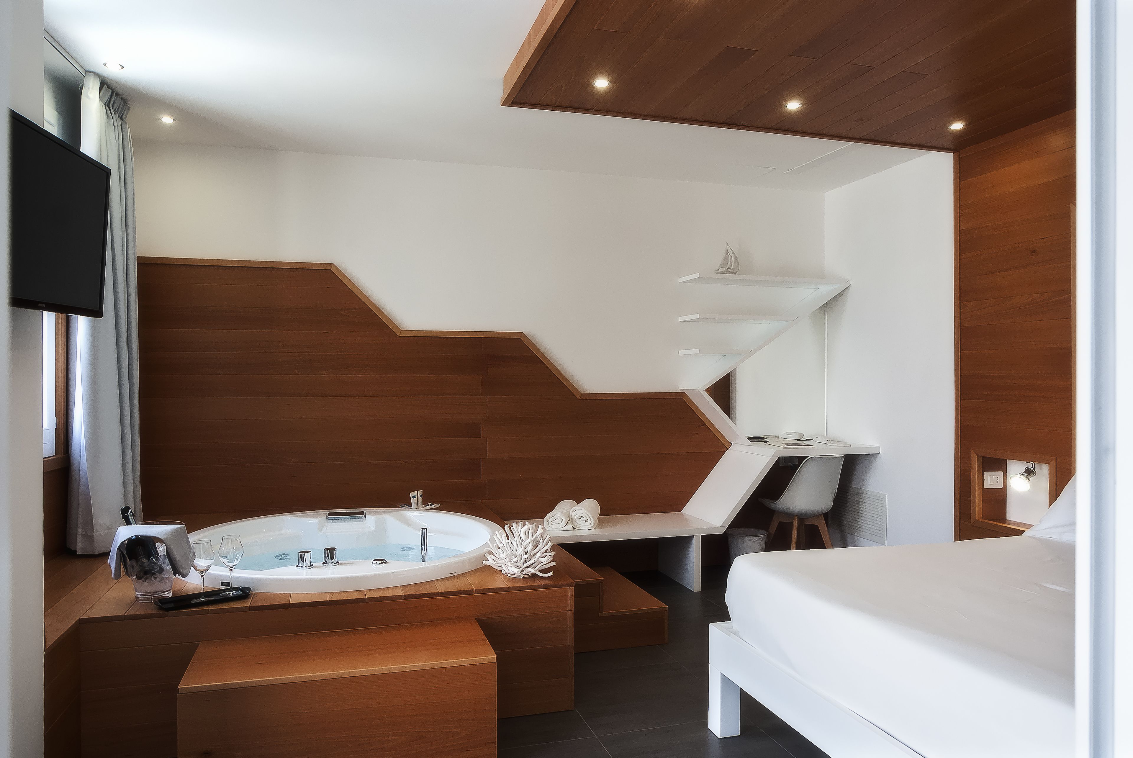 Quarto de hotel moderno com parede de destaque em madeira, uma banheira grande, uma escrivaninha e uma cama.
