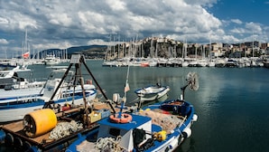A marina with boats docked, a small boat with a winch, and a building on a cliff in the background. - La Sciabica (Agropoli)