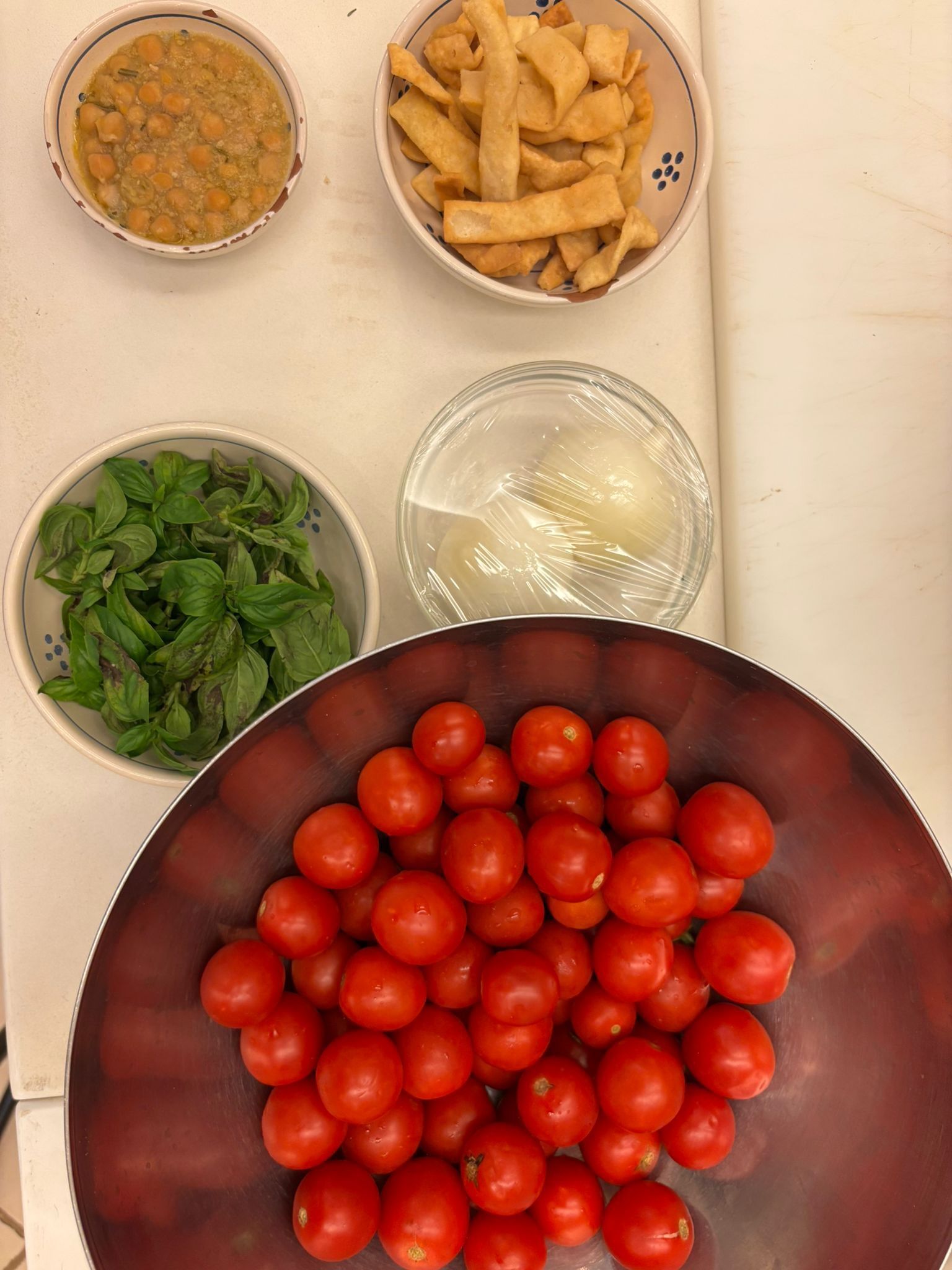 Une table sur laquelle on trouve divers aliments, notamment un bol de tomates cerises, un bol de légumes verts, un bol de pois chiches et un bol de frites.