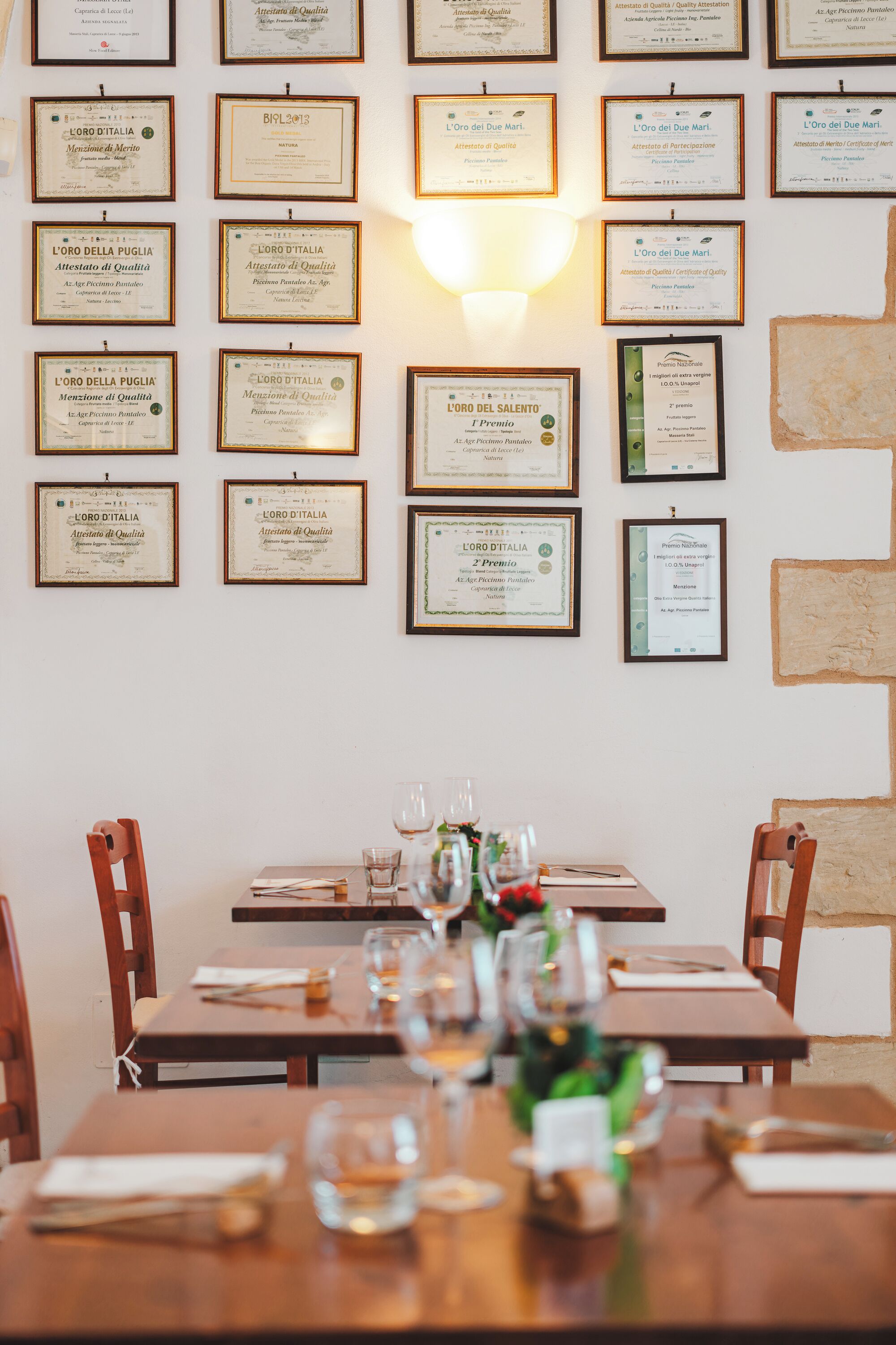 A restaurant interior with a long table set for dining, framed certificates on the wall, and a brick wall.
