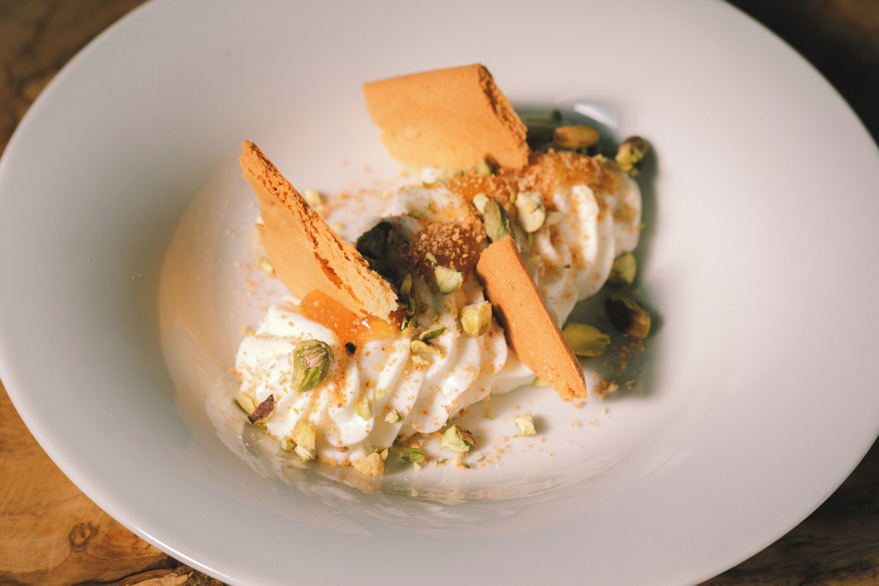 Un postre con crema batida, nueces y un trozo de pastel sobre un plato blanco.