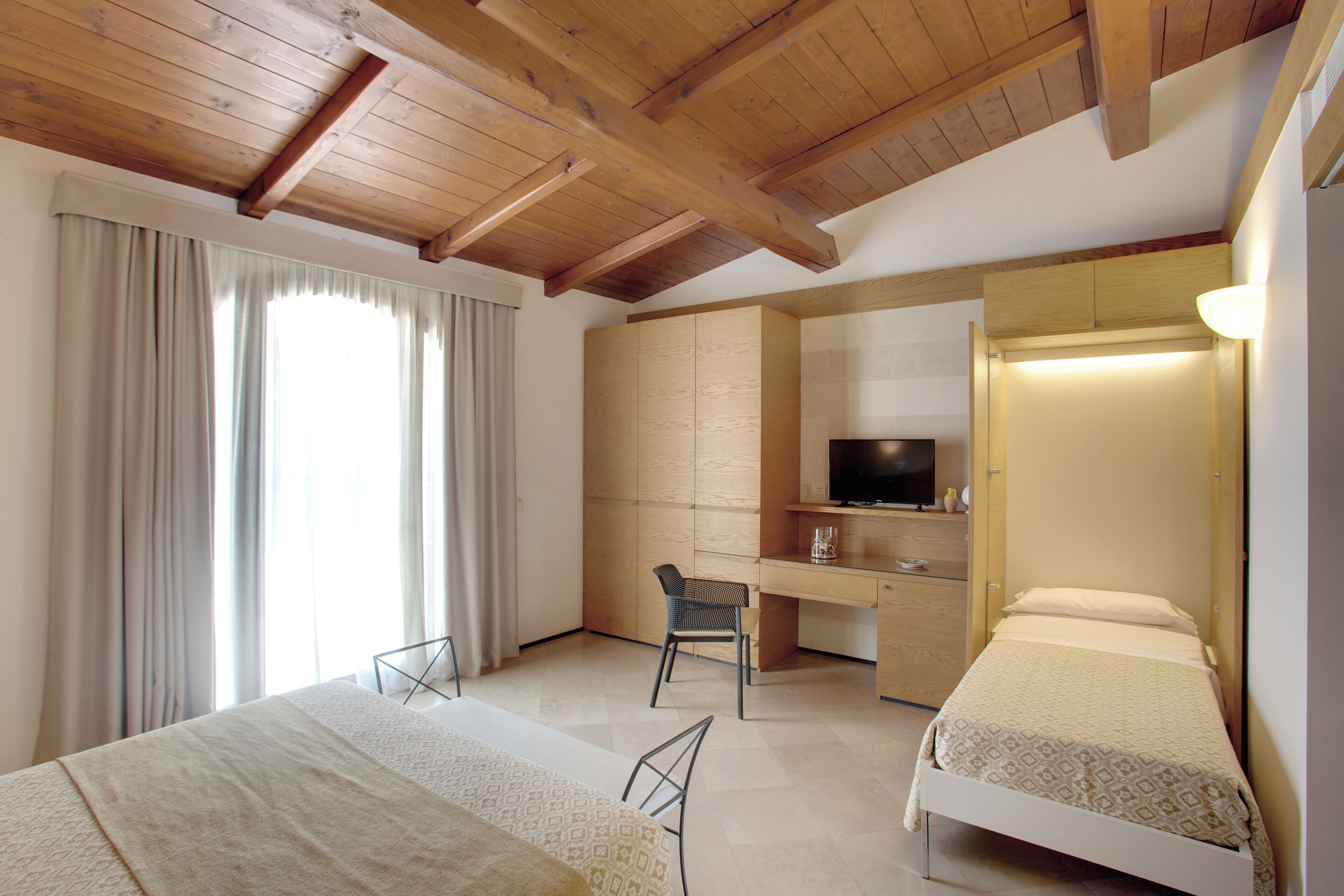 Ein Hotelzimmer mit Holzboden, einem Bett, einem Schreibtisch mit Stuhl, einem Fernseher und einem Kleiderschrank.