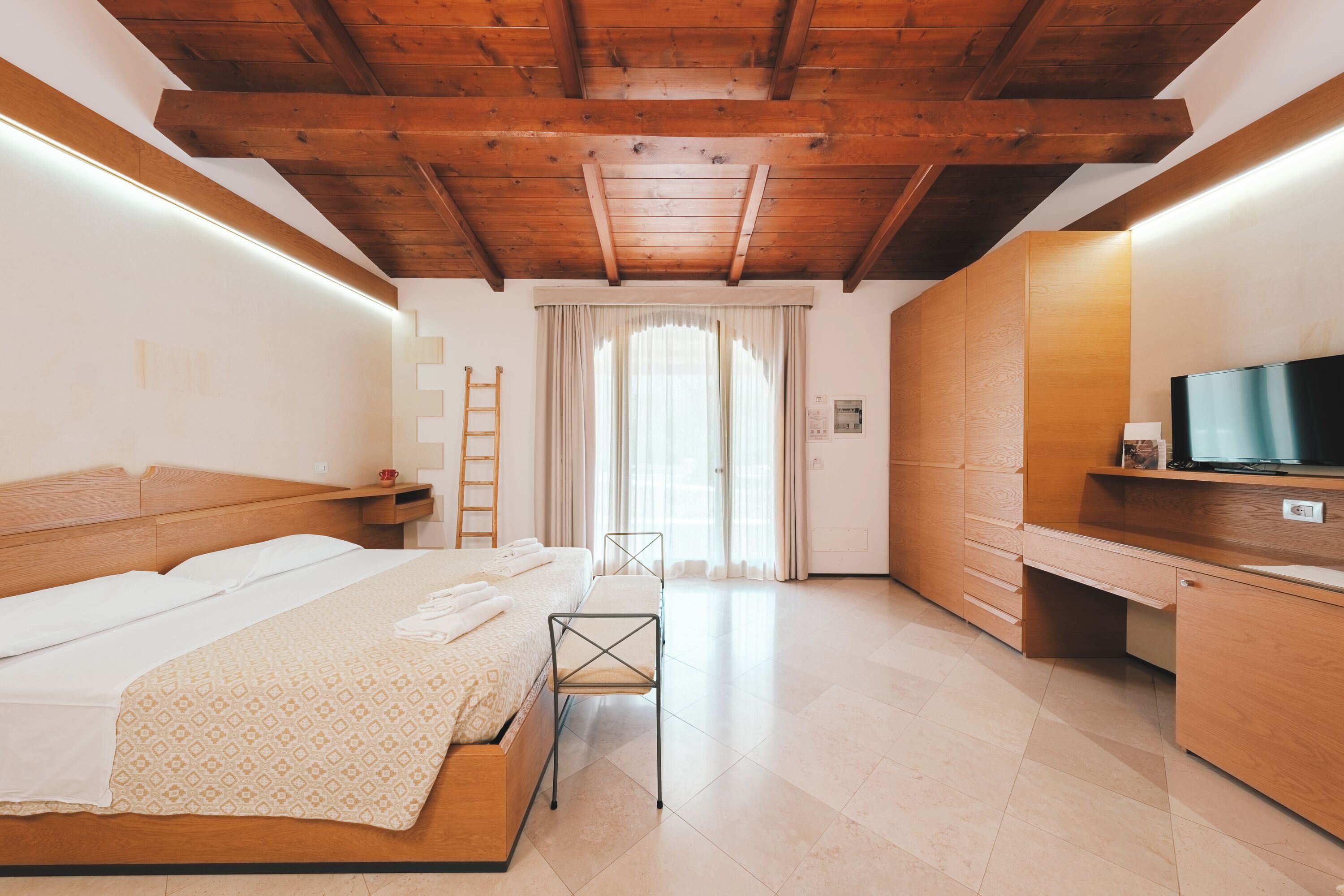 A bedroom with a wooden ceiling, a bed, a desk, and a television.